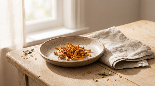 Dried orange cordyceps mushrooms in a speckled ceramic dish on a wooden table in soft morning light